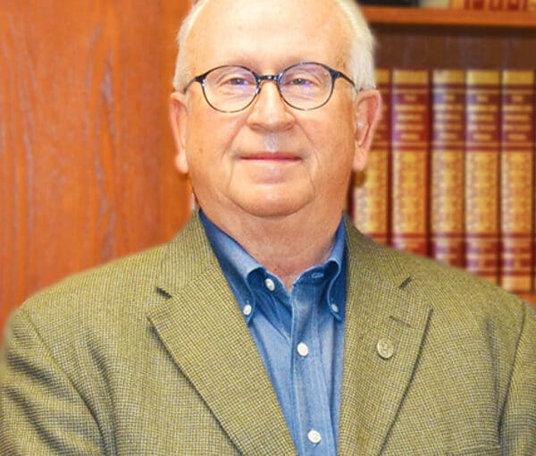Dr. James Fox, professional headshot in office with law books, wearing glasses and tan blazer over blue shirt