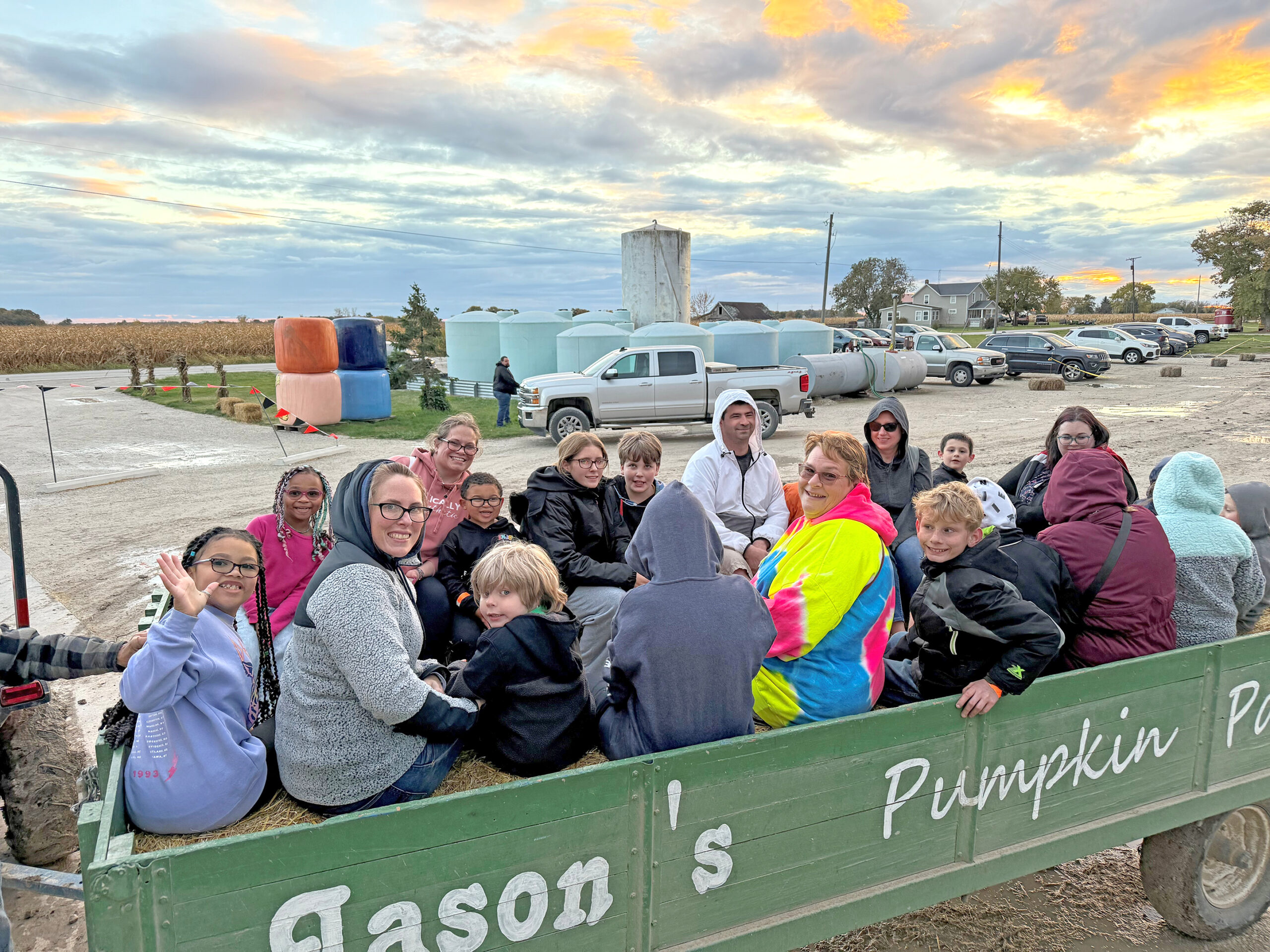 Group of children and adults riding in a green wagon labeled 