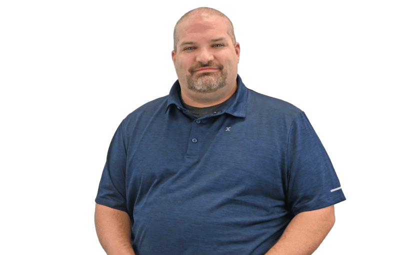 Jason Young, a staff member in a blue polo shirt and gray pants, seated for a professional portrait