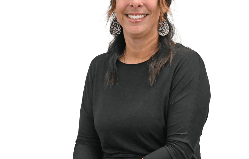 Jennifer Rodriguez, Service and Support Administrator, smiling at camera wearing black long-sleeve shirt and jeans with leopard print earrings