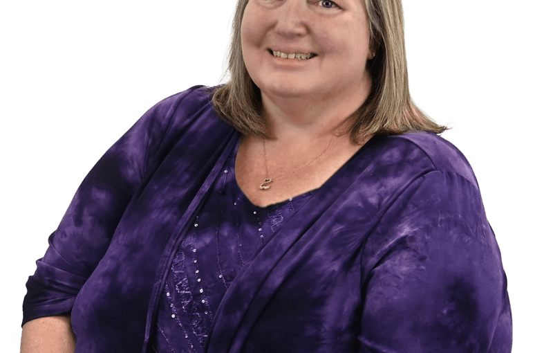 Michele Mong, Administration Business Manager, smiling in professional portrait wearing purple velvet blazer against white background