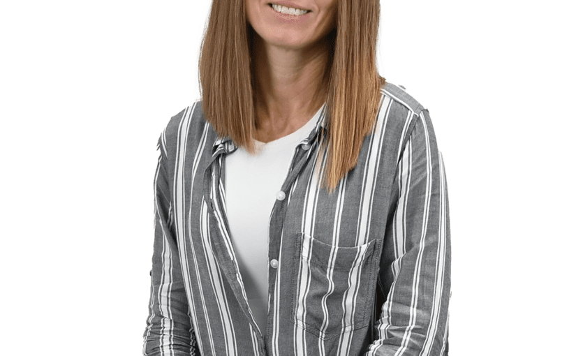Michelle Snyder, Administration HR staff member, smiling at camera wearing gray striped button-up shirt