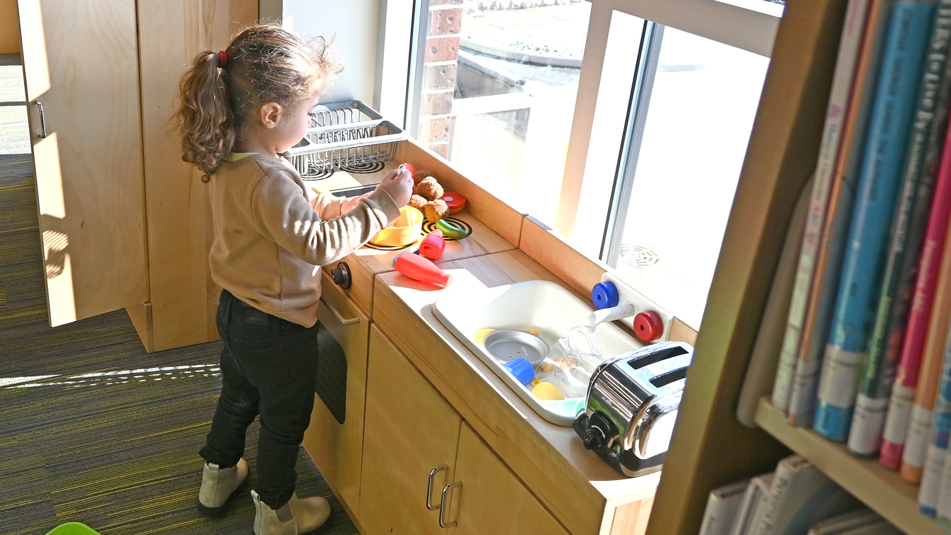 Young child with curly hair playing with toys at a library windowsill during early intervention activities in Sandusky County, Ohio