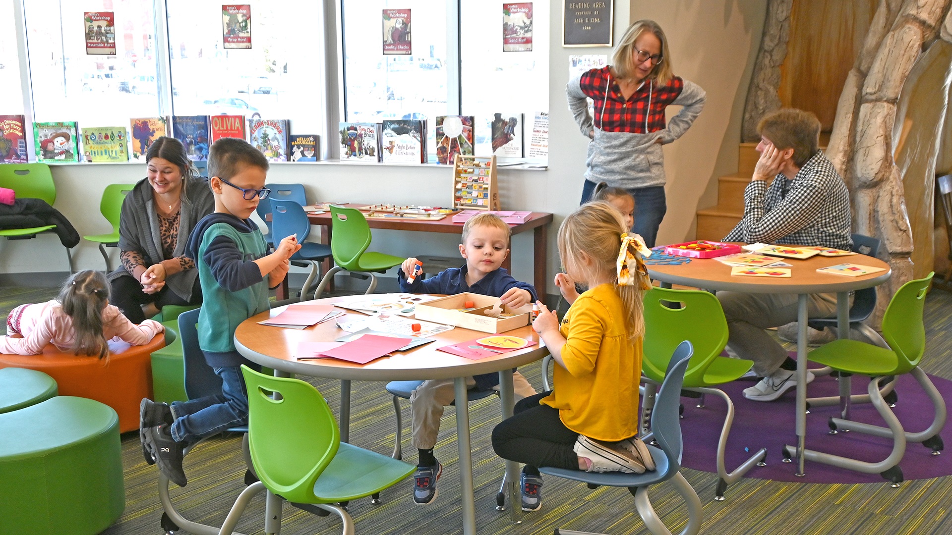 Children and adults engaged in interactive activities at a developmental disability services program in Sandusky County, Ohio, with colorful tables and chairs in a bright classroom library setting