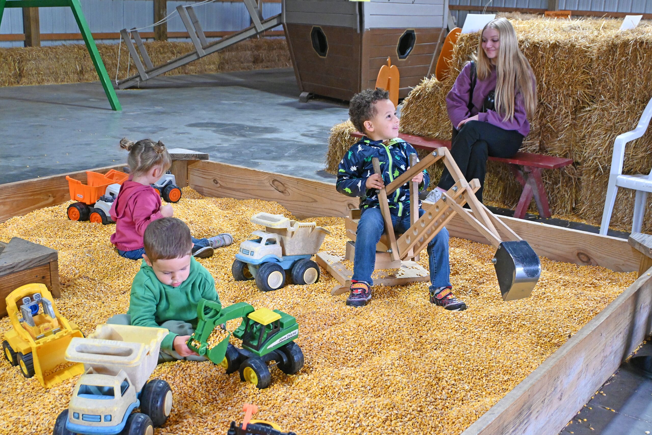 Children playing in a sensory sandbox with toy construction vehicles and wooden climbing equipment at an outdoor play area