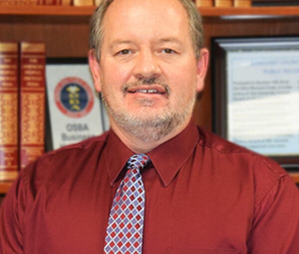 Shane Dyer, professional man in burgundy shirt and patterned tie standing in front of law books and office setting in Sandusky County, Ohio