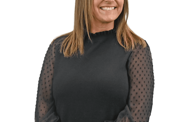 Tasha Tysiak, SSA Manager, smiling at camera wearing black top with sheer polka dot sleeves and blue jeans
