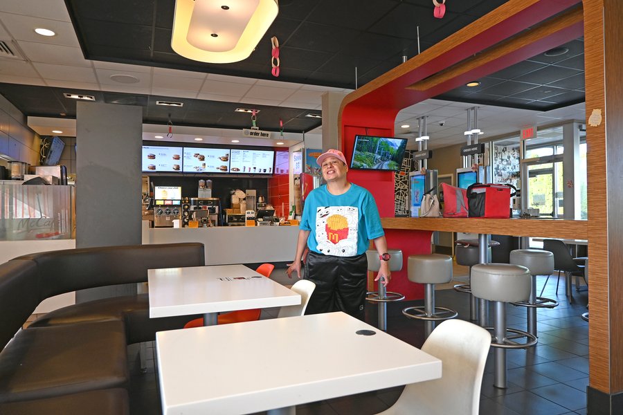 Woman in McDonald's uniform and cap standing in modern fast-food restaurant dining area with white tables and red accent walls