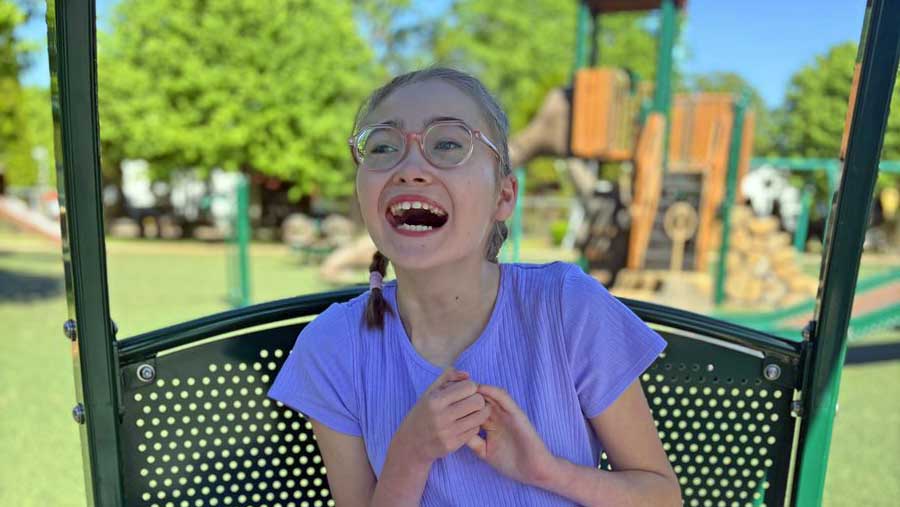 Smiling girl wearing glasses and purple shirt sits in green playground equipment at park in Sandusky County Ohio